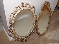 Two ornate framed mirrors side-by-side on carpet; ivory openwork carved frame and gilded shaped frame