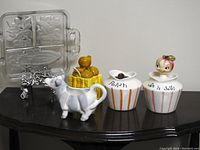 Full view of all items showing the condiment jars, cow creamer, basket with fruit, and intaglio glass tray on stand.