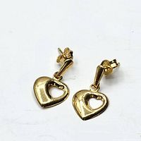 Pair of 14k gold heart-shaped earrings with a smaller heart cut-out in the center, showing front and side angles.