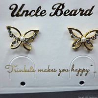 Front view of a pair of gold plated butterfly-shaped earrings with cubic zirconia stones and central pearls on a branded display card.