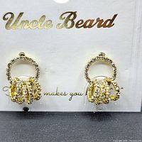 Front view of the gold plated stainless steel earrings with clear cubic zirconia stones set around a circular hoop and decorative dangle, attached to a white cardboard backing branded Uncle Beard.