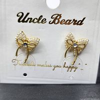 Top-down view of both butterfly earrings on original Uncle Beard branded card packaging, showing pearl embellishment and central CZ stone.