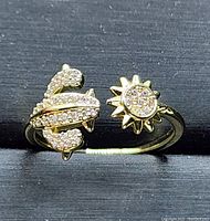 Front close-up of a gold plated adjustable ring with two CZ-accented decorative ends, a sun shape and an abstract knot shape.