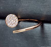 Close-up image of rose gold plated adjustable ring with round cluster of cubic zirconia stones on one end, showing top view