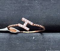Close-up photo of rose gold plated ring featuring CZ 'H' initial on black fabric background.