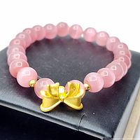 Rose quartz bead bracelet displayed on black surface, showing round pink beads with gold bow accent.