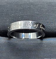 Close-up of polished stainless steel ring band with 'Angel of love' engraved and single cubic zirconia stone.
