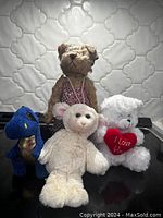 Four small stuffed animals including teddy bear, blue dinosaur, white sheep, and white plush with heart pillow