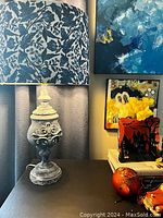 Table lamp with chalk paint base and blue floral decoupaged shade, on black surface next to colorful items and abstract paintings.