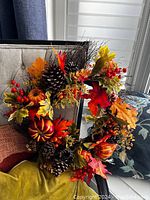 Full view of the fall wreath showing pine cones, pumpkin decorations, red berries, and colorful fall leaves.