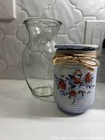 Photo of clear glass vase and hand painted candle jar showing floral design and twine around jar neck.