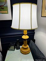 Full view of the yellow painted table lamp sitting on a side table next to a cordless phone and a TV remote.