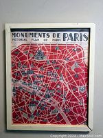 Front view of the framed Monuments de Paris poster showing a detailed map of Paris with monuments illustrated and a white frame with visible damage.