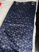 Full view of one navy blue window panel with silver geometric cube pattern and three large silver grommets