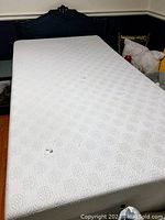 Photo of a used white single bed mattress showing two damaged spots on the surface with fabric worn through, placed on a bed frame.