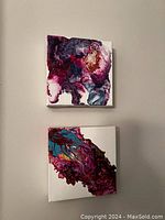 Two small square canvases hung on wall showing abstract acrylic pour art with fluid, marbled color patterns