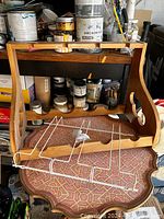 Image showing a light wood wine rack placed upside down on a table, featuring curved side panels and scalloped horizontal slots for bottles, next to a white metal IKEA wine glass holder designed to hold glasses upside down.