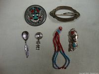 Full view of assortment of Native American themed jewelry including brooches, earrings, pendant, and beaded necklace on white background.