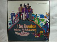 Front of framed Beatles Yellow Submarine vinyl album featuring colorful illustrated cover with Beatles members and animated characters, showing some fading and minor wear.