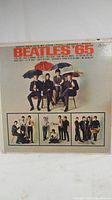 Front album jacket with classic Beatles '65 artwork featuring members with umbrellas and tabloid style photos below.