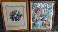 Photo showing both the framed Native American mask with feathers and the framed French advertising poster side by side.