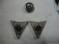 Pair of sterling silver triangular collar tabs and a silver button snap with turquoise and coral inlay displayed on a white cloth.