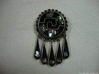 Front view of Native American silver pin or pendant showing inlaid mother-of-pearl and onyx with dangling teardrop shapes.