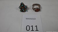 Pair of Native American style rings placed next to a MaxSold number card, showing the full view of both rings