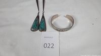 Photo showing two silver bolo tie end pieces with turquoise inlay and a silver cuff bracelet with turquoise and coral inlay on white background with lot number card