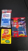 Photo showing three sealed sports card packs laid flat on a black surface: NFL Pro Set, Fleer Basketball 1990, and Topps 1994 Baseball.