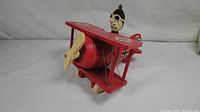 Red wooden tri-plane shaped vintage music box depicting The Red Baron character with skull pilot head and cream-colored propeller in the front.