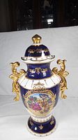 Full view of vintage cobalt blue porcelain vase with ornamental gold handles and lid with gold finial.