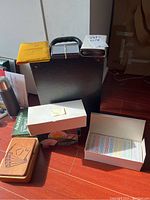 Lot displayed on floor with a black briefcase in background, including white box with card decks, wooden box with carved card design, AutoBridge box, and instruction booklet.