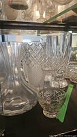 Photo showing a variety of vintage crystal vases including a large curved clear glass vase, two medium cut crystal vases with diamond patterns, and a small cut glass vase.