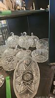 Cluster of crystal candy dishes with lids and various pressed glass bowls showing detailed cut patterns and reflective clarity.