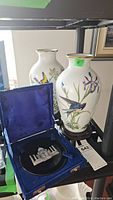 Two porcelain vases and open blue velvet box with inlaid stone plate on shelf