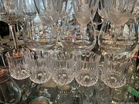 Etched floral pattern stemmed glasses in front row, textured short tumblers in front, all clear glass, on mirrored shelf.
