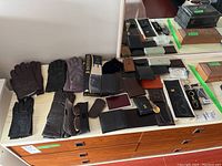 Overview of all gloves, wallets, coin purses, key holders, and sunglasses in case displayed on a white surface.