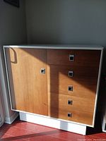 Front view of dresser showing white frame, wood veneer drawers, cabinet door closed, square metal pulls