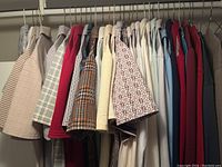 Hanging rack showing a variety of men's vintage dress and casual shirts with different colors and patterns including plaid, houndstooth, red and white patterned shirts.