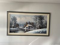 Front view of framed winter landscape panoramic painting with snow-covered trees and watermill by river