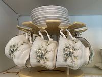 Eight Paragon china cups hanging on a mug tree with matching saucers on top, showing floral and silver decorate edges.