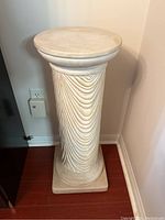 Front angled view of taller ceramic pedestal with fluted design and square base, showing the overall form and surface details.