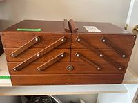 Front view of the wooden sewing cabinet showing multiple fold-out compartments and metal knobs.