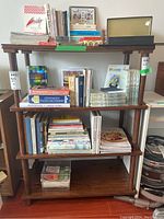 Full frontal view of the wooden pressboard shelf, loaded with various books and magazines which are not included in the lot.