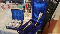Silverplate egg cup set with six egg cups in a lined blue velvet case and two silverplate champagne flutes in a blue velvet case on a chair