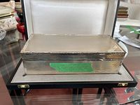 Front view of silver keepsake box in storage case showing guilloche pattern on lid and floral border engraving