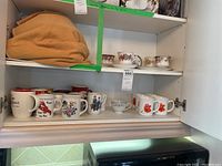 Shelf with two Royal Albert cups and plates on the middle right and a shelf of mugs below, including red poppy and other floral designs, and humorous text mugs.
