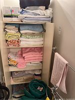 Cabinet interior showing multiple folded towels organized on shelves with a rolled green sleeping bag on the floor.