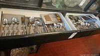Top view of a drawer with trays containing stainless steel spoons, forks, and knives with different handle patterns.